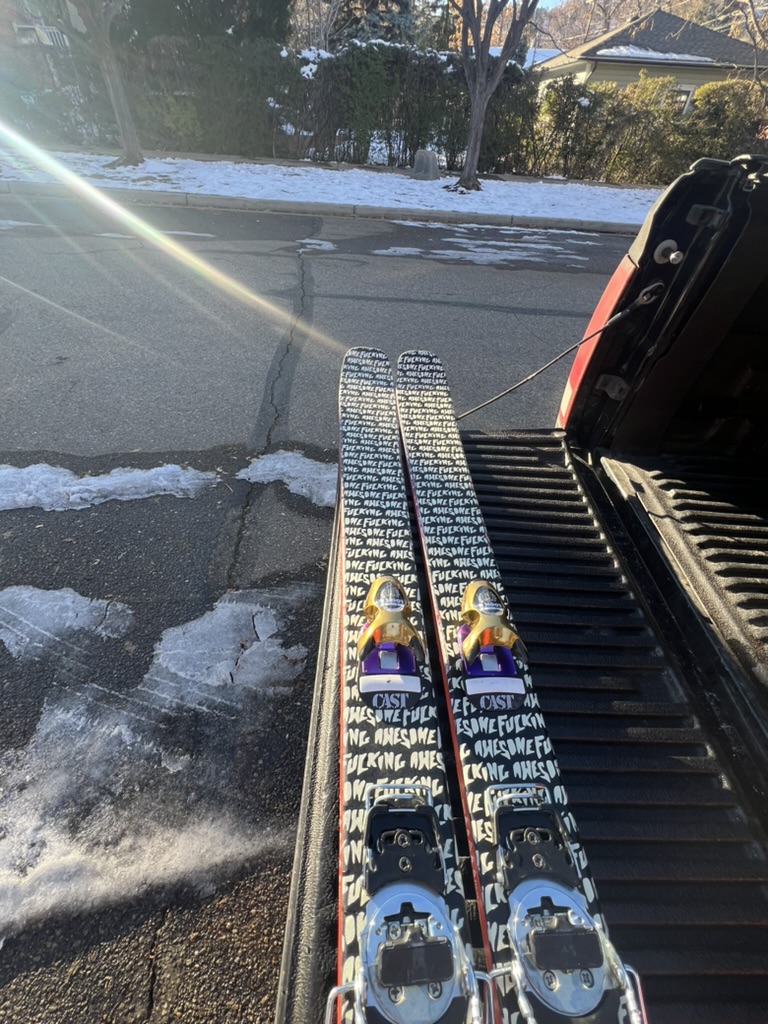 Skis with hand lettered topsheets lying in the bed of a pickup on a snowy day