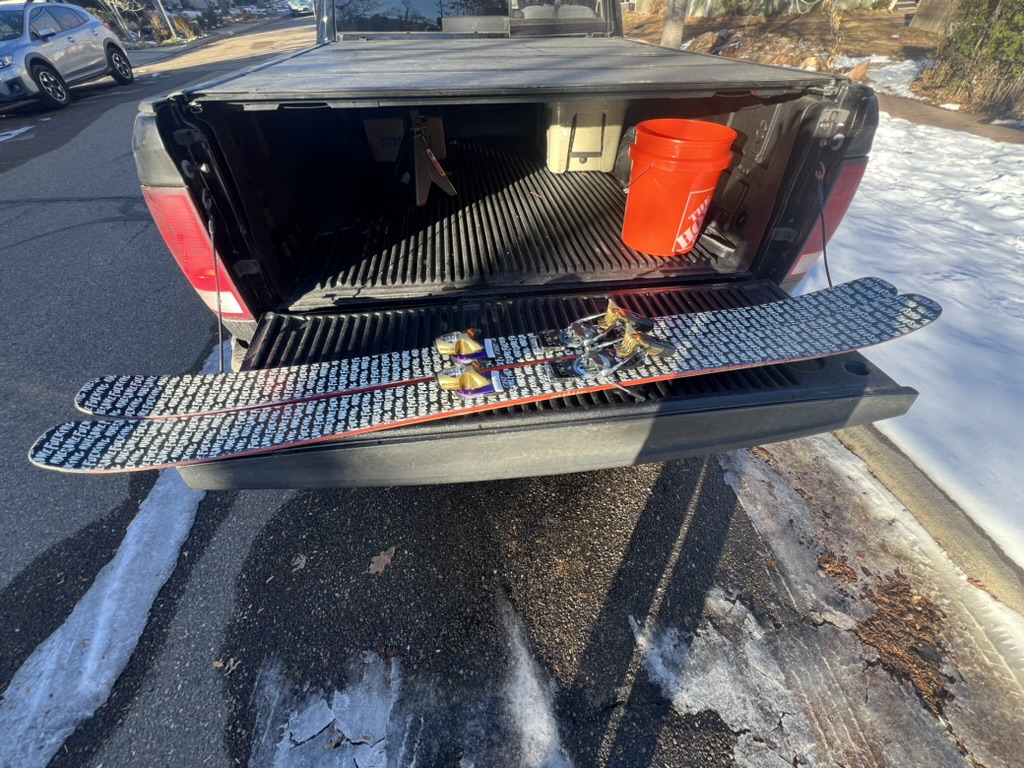 Skis resting across the open tailgate of a pickup, painted topsheets facing up